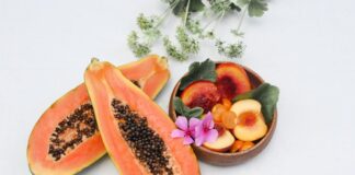 Colorful composition of sliced papaya and peaches with flowers on white background.