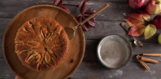 A homemade apple cake surrounded by autumn leaves and spices, top view.