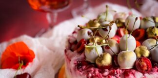 A luxurious cherry cheesecake topped with golden white chocolate drizzled cherries on a rustic tabletop.