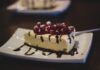 Slice of cheesecake topped with berries and chocolate drizzle on a plate.