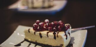 Slice of cheesecake topped with berries and chocolate drizzle on a plate.