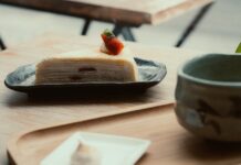 A slice of crepe cake topped with a strawberry, served on a wooden table.