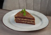 A tempting chocolate layer cake slice with mint garnish on a white plate.