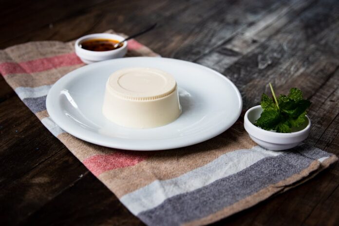 Descubra o Segredo da Bavaroise Perfeita e Surpreenda! Delicious panna cotta served with fresh mint and sauce on a rustic table setting.