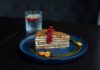 Elegant layer cake with red currants and physalis, served on a blue plate, showcasing gourmet dessert art.
