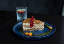 Mille-feuille Francês: Descubra o segredo autêntico Elegant layer cake with red currants and physalis, served on a blue plate, showcasing gourmet dessert art.