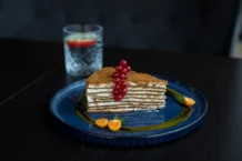 Mille-feuille Francês: Descubra o segredo autêntico Elegant layer cake with red currants and physalis, served on a blue plate, showcasing gourmet dessert art.