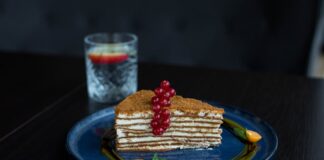 Elegant layer cake with red currants and physalis, served on a blue plate, showcasing gourmet dessert art.