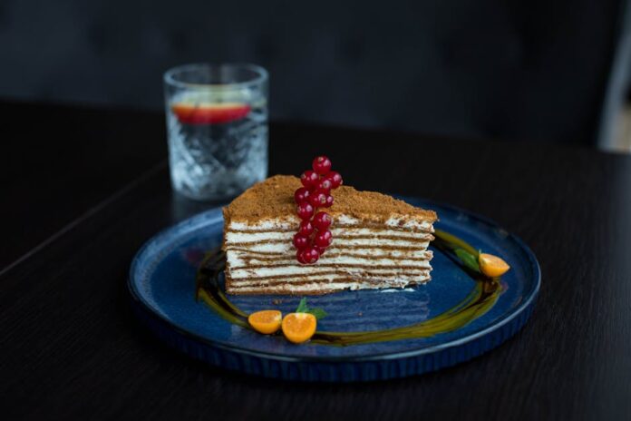 Descubra o Segredo do Autêntico Mille-feuille Francês Elegant layer cake with red currants and physalis, served on a blue plate, showcasing gourmet dessert art.