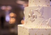 Close-up of a tiered wedding cake with detailed fleur-de-lis and hummingbird decorations.