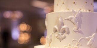 Close-up of a tiered wedding cake with detailed fleur-de-lis and hummingbird decorations.
