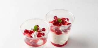 Two delicious red berry parfaits with cream, mint garnish in clear cups.