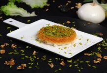 Kunafa: Uma delícia oriental Close-up of mouthwatering Arabic Kunafa topped with chopped pistachios.