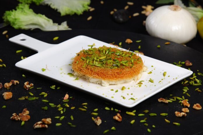 Descubra os Segredos da Kunafa: Uma Delícia Oriental Close-up of mouthwatering Arabic Kunafa topped with chopped pistachios.