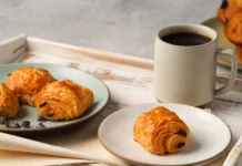 Croissant doce: Perfeito em casa Enjoy a delightful breakfast with fresh croissants and a cup of coffee served on a rustic tray.