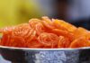 Close-up photo of crispy, orange Indian jalebi served in a decorative stainless steel bowl.