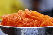Jalebi: Descubra a tradição e o sabor único Close-up photo of crispy, orange Indian jalebi served in a decorative stainless steel bowl.