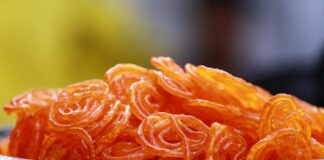Close-up photo of crispy, orange Indian jalebi served in a decorative stainless steel bowl.