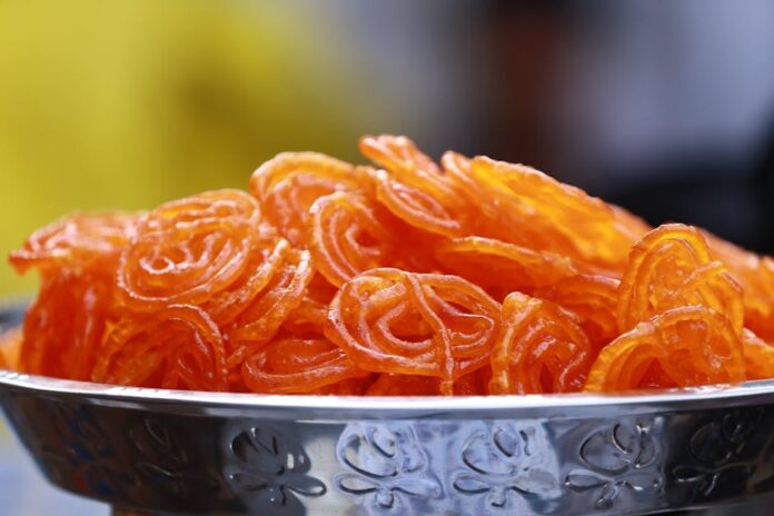 Jalebi: Descubra a Tradição e o Sabor Único Desta Doçura Close-up photo of crispy, orange Indian jalebi served in a decorative stainless steel bowl.