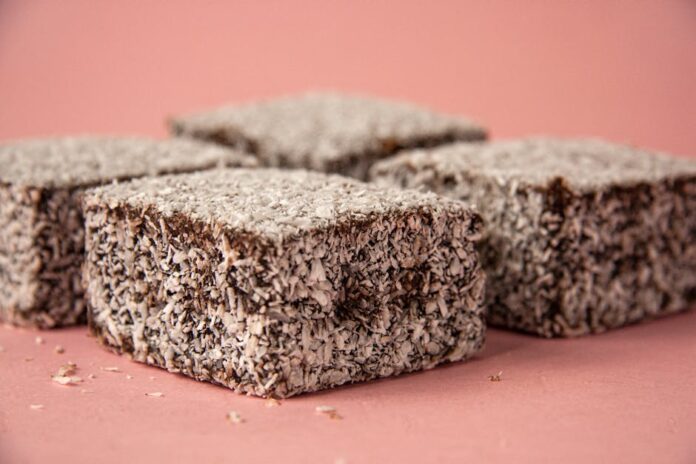 Lamington: Descubra o Segredo do Doce Australiano Irresistível Close-up of scrumptious lamington cakes with desiccated coconut on a pink background.