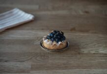Paris-Brest: Descubra o segredo por trás desse doce irresistível Tasty blueberry tart with powdered sugar on a wooden table in Berlin cafe. Perfect dessert for sweet tooth lovers.
