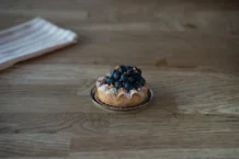 Paris-Brest: Descubra o segredo por trás desse doce irresistível Tasty blueberry tart with powdered sugar on a wooden table in Berlin cafe. Perfect dessert for sweet tooth lovers.