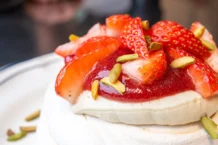 Pavlova: Descubra o segredo por trás da sobremesa perfeita Close-up of a pavlova topped with fresh strawberries and pistachios, perfect for gourmet breakfast ideas.