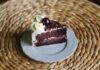 Close-up of a slice of Black Forest cake with cream, cherry, and chocolate on a woven background.