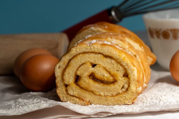 Receita de bolo caseiro para pequeno-almoço: segredo revelado! Close-up of a freshly baked roll cake with baking ingredients.