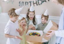 Receita de bolo para crianças: Segredo para encantar Joyful kids celebrating a birthday with a colorful cake and party hats indoors.