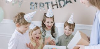 Joyful kids celebrating a birthday with a colorful cake and party hats indoors.