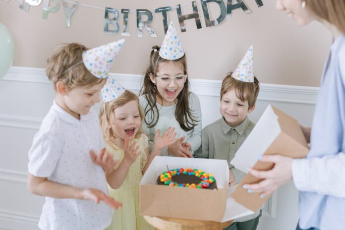 Receita de bolo para crianças: segredo para encantar! Joyful kids celebrating a birthday with a colorful cake and party hats indoors.