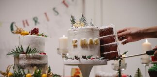 A hand cuts a slice from a beautifully decorated Christmas cake adorned with festive decor indoors.