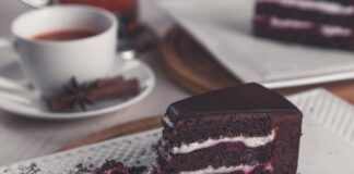 Closeup of a rich chocolate cake slice on a plate with a tea cup in the background.