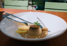 Panna Cotta: Descubra o segredo Coffee panna cotta dessert garnished with mint, served with pineapple and pine nuts in an outdoor setting.