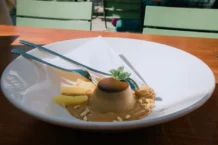 Panna Cotta: Descubra o segredo Coffee panna cotta dessert garnished with mint, served with pineapple and pine nuts in an outdoor setting.