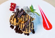 Profiteroles: Surpreenda com esta delícia Sumptuous profiteroles topped with chocolate sauce and berries, presented on a white dish.