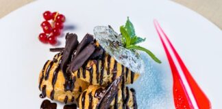 Sumptuous profiteroles topped with chocolate sauce and berries, presented on a white dish.