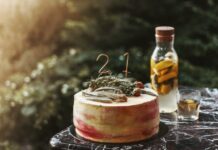 Elegant rustic birthday cake with herbal decor and infused water on marble table, outdoors.