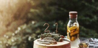Elegant rustic birthday cake with herbal decor and infused water on marble table, outdoors.