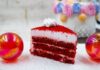 A vibrant red velvet cake slice with frosting, surrounded by festive colorful decorations.
