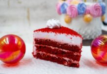 Red Velvet: Surpreenda o paladar A vibrant red velvet cake slice with frosting, surrounded by festive colorful decorations.