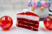 Red Velvet: Surpreenda o paladar A vibrant red velvet cake slice with frosting, surrounded by festive colorful decorations.