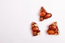 Toffee: Descubra os segredos do doce perfeito Close-up of almond brittle pieces on a white backdrop, offering tempting texture.